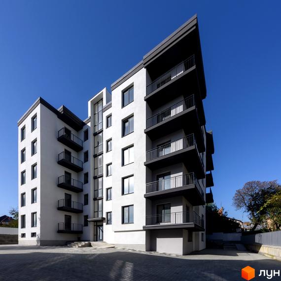 Зовнішній вигляд новобудови на вул. Козачука, 27а, з білими фасадами та темними балконами на фоні блакитного неба. Прибудинкова територія з бруківкою та огорожею.