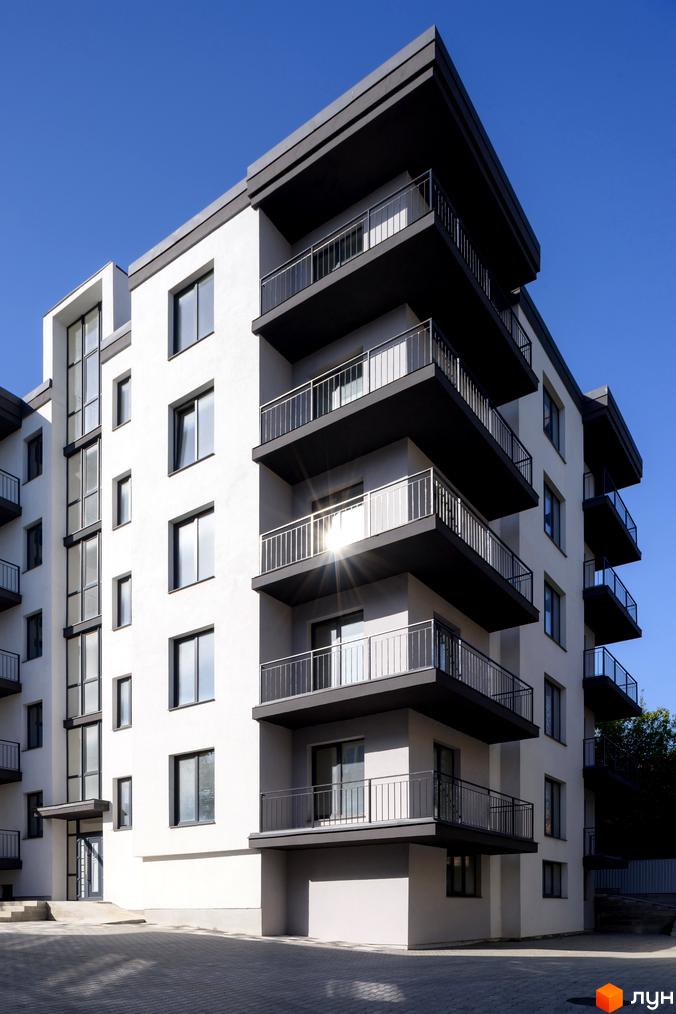 Зовнішній вигляд будинку на вул. Козачука, 27а, з балконами та вікнами на фоні блакитного неба. На прибудинковій території видно бруківку та сходи.