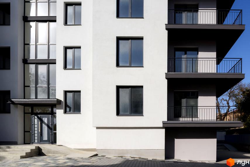 Фасад житлового комплексу на вул. Козачука, 27а, з балконами та вікнами. Прибудинкова територія з бруківкою та сходами.