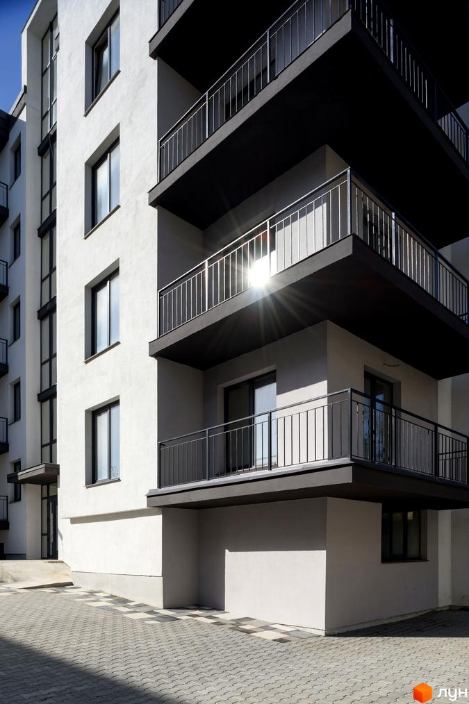 Зовнішній вигляд новобудови на вул. Козачука, 27а з балконами та вікнами. Прибудинкова територія з бруківкою.