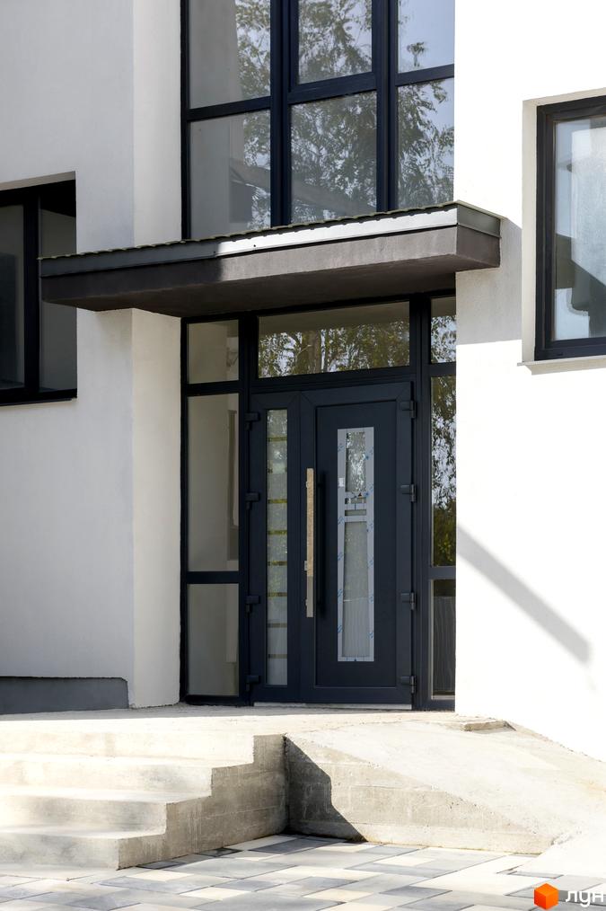 Вхідна група житлового комплексу на вулиці Козачука, 27а. Сучасний дизайн фасаду з великими вікнами та темними дверима, облаштований пандусом та сходами.