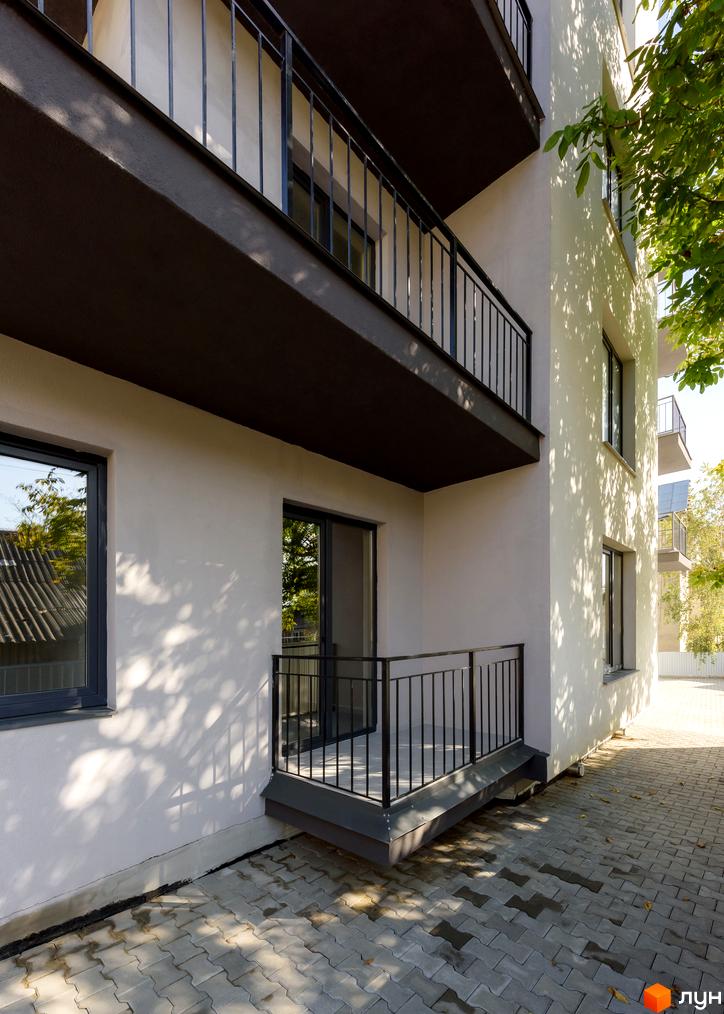 Зовнішній вигляд новобудови на вул. Козачука, 27а, з балконами та вікнами. Прибудинкова територія вимощена плиткою.