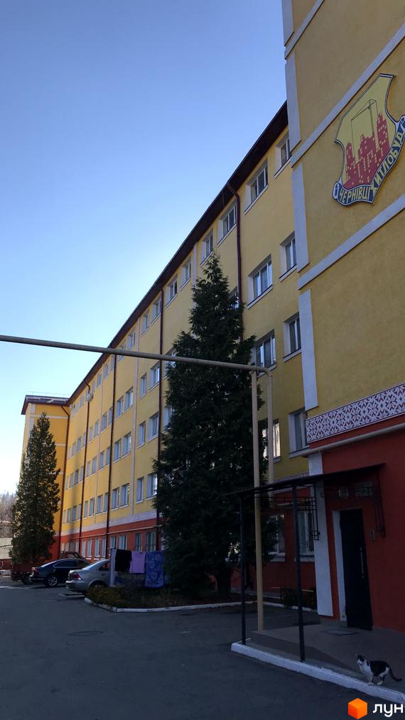 Житловий комплекс на вулиці Вокзальна (Юрія Гагаріна), 54а, з жовтим фасадом, білими вікнами та червоним цоколем. Перед будинком ростуть ялинки та припарковані автомобілі.