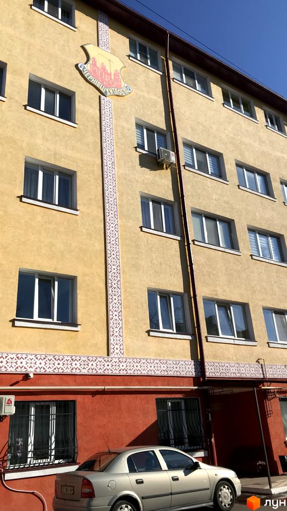 Фасад житлового комплексу на вул. Вокзальна (Юрія Гагаріна), 54а. Будинок має жовтий колір стін з декоративними елементами та червоний цоколь. Поруч припаркований сріблястий автомобіль.