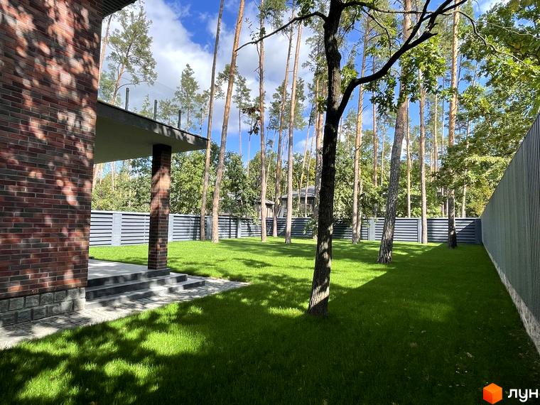 Котеджне містечко КМ Лісові Плюти. Цегляний будинок з терасою та доглянутою зеленою ділянкою з деревами.