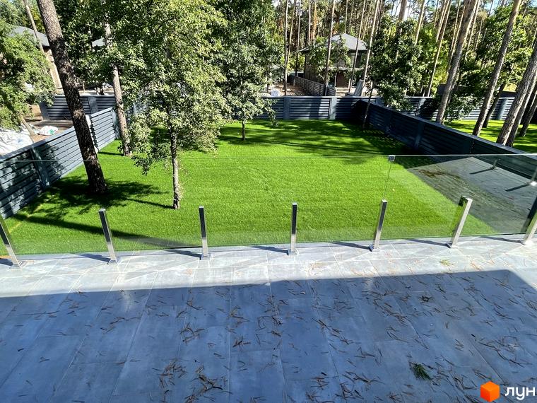 Котеджне містечко КМ Лісові Плюти: зелений газон та скляна огорожа на прибудинковій території. Будинки оточені деревами.