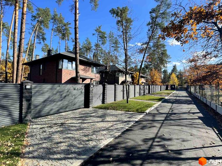 Котеджне містечко КМ Лісові Плюти. Фасад будинку з червоної цегли та сірий паркан з автоматичними воротами.