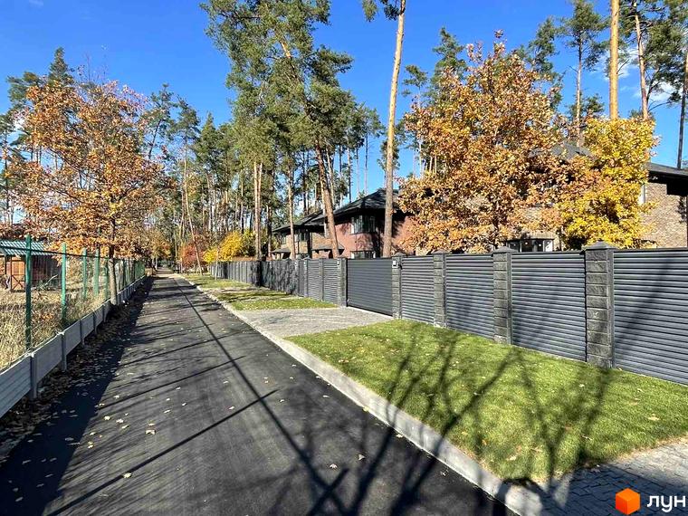Котеджне містечко КМ Лісові Плюти: асфальтована дорога з газоном та парканом. Навколо будівель ростуть дерева з жовтим листям.