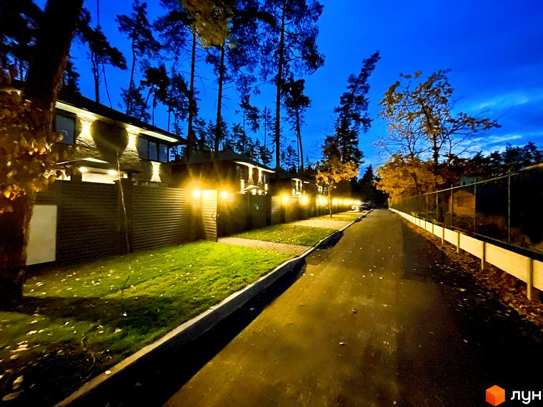 Котеджне містечко КМ Лісові Плюти. Зовнішній вигляд будинків з підсвіткою та охайною прибудинковою територією з газоном та дорогою.