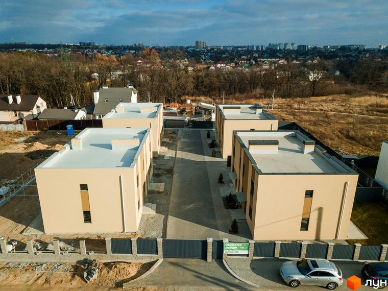 Зовнішній вигляд будинків котеджного містечка КМ My Land, з доглянутою прибудинковою територією та парканом.