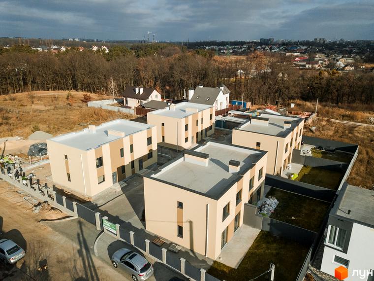 Котеджне містечко КМ My Land: фасади будинків світло-бежевого кольору з темними вікнами, прибудинкова територія з зеленими газонами та парканом.