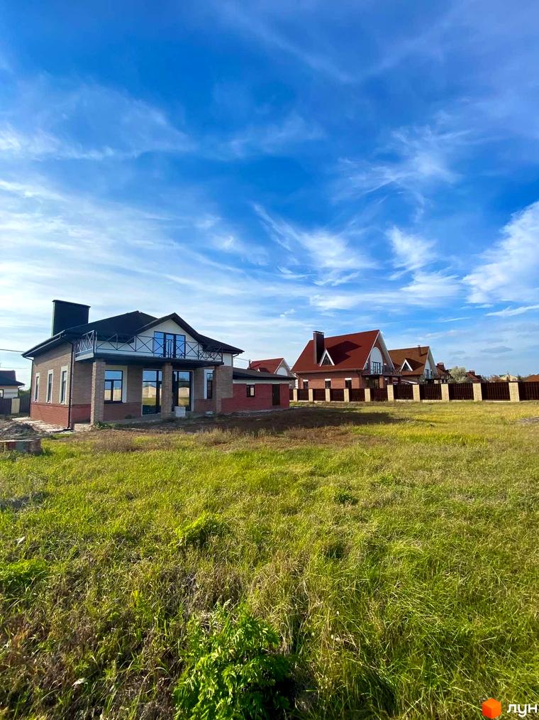 Котеджне містечко Барвіта: двоповерхові будинки з червоної цегли та балконами під сірим дахом, розташовані на зеленій ділянці з травою під блакитним небом.