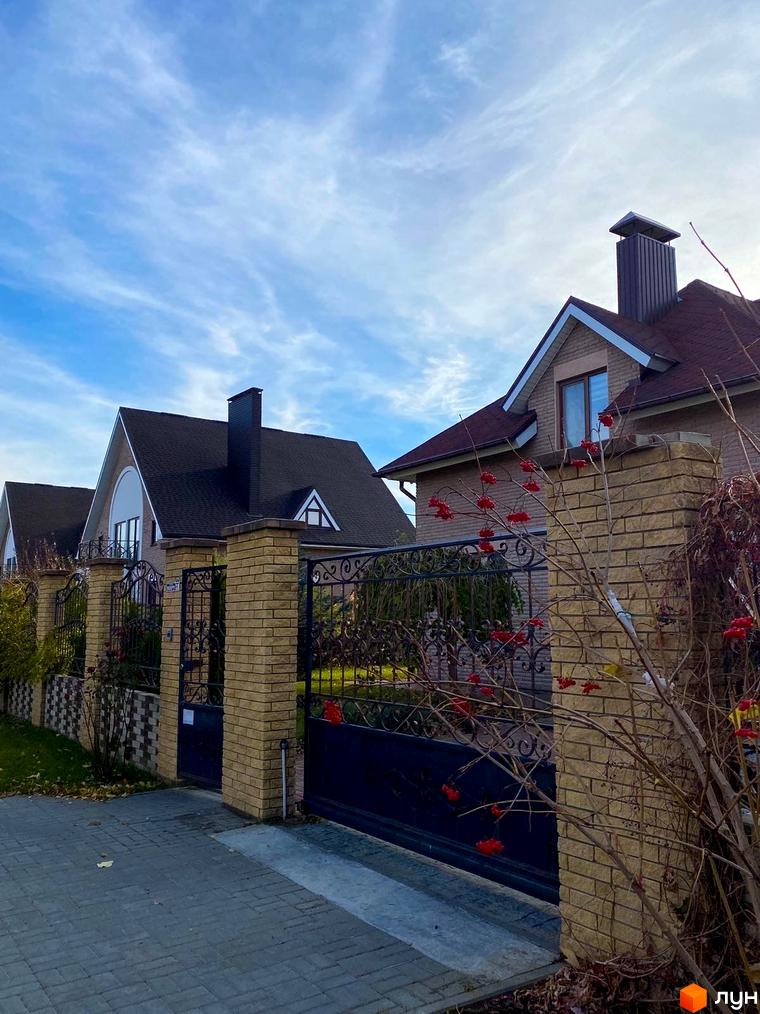 Котеджне містечко КМ Барвіта: фасади будинків з темною черепицею та цегляними елементами, ковані ворота та огороджена територія.