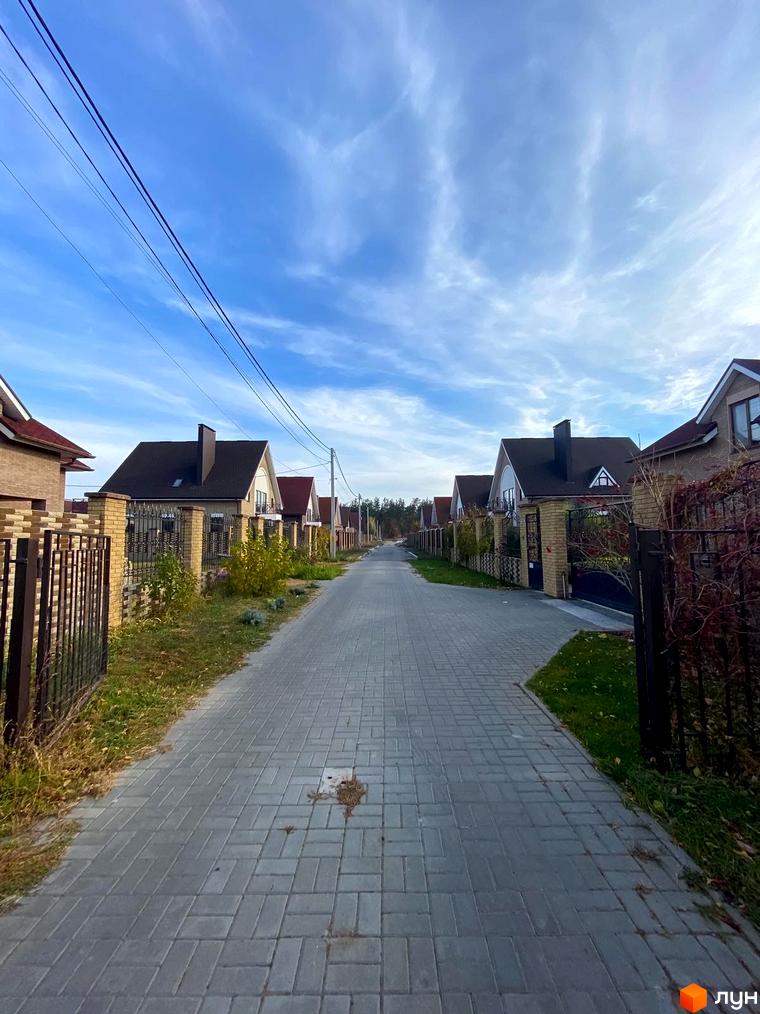 Котеджне містечко КМ Барвіта: вулиця з бруківки з будинками та парканами. Навколо зелена трава та дерева.