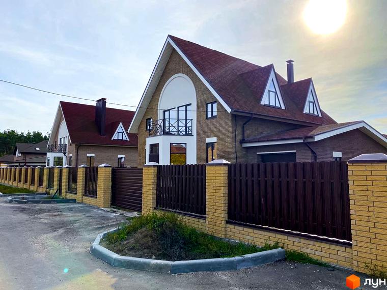 Котеджне містечко КМ Барвіта: двоповерхові будинки з червоним дахом та цегляним фасадом, огороджені парканом. Прибудинкова територія з дорогою та зеленими насадженнями.
