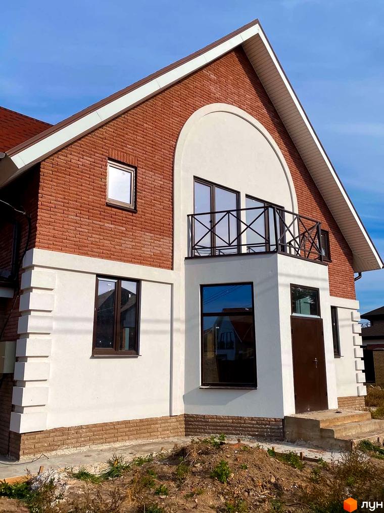 Котеджне містечко КМ Барвіта: двоповерховий будинок з червоної цегли та білої штукатурки, балконом та коричневими вікнами.
