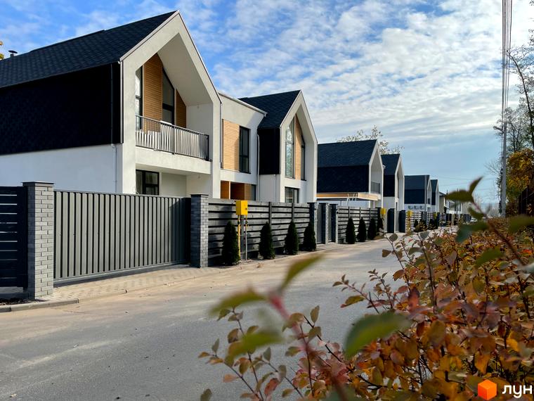 Котеджне містечко КМ Loft City: сучасні будинки з чорними та білими фасадами, дерев'яними вставками та великими вікнами. Огороджена територія з парканом та зеленими насадженнями.