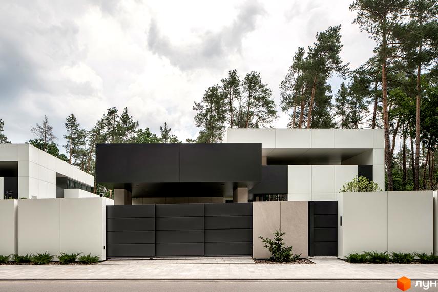 Фасад котеджного містечка 3L Residences з великими чорними та білими панелями. Перед будинком розташована огорожа, а на задньому плані видніються дерева.