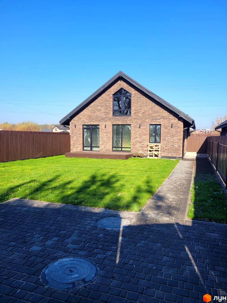 Зображення будинку з червоної цегли в Котеджному містечку Одноповерховий Київ - Шевченкове. Перед будинком зелений газон та доріжка з тротуарної плитки.