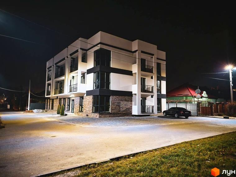 Зображення фасаду Житлового комплексу Premium House вночі. На передньому плані асфальтована дорога та припаркований автомобіль.