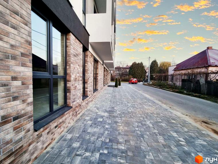 Зображення фасаду та тротуару Житлового комплексу Преміум Хаус. Вигляд на дорогу з червоним автомобілем та будинки на задньому плані.