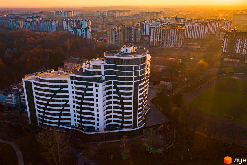 Зображення житлового комплексу Parus. Багатоповерхова будівля з горизонтальними смугами, поруч зелена зона та стадіон.