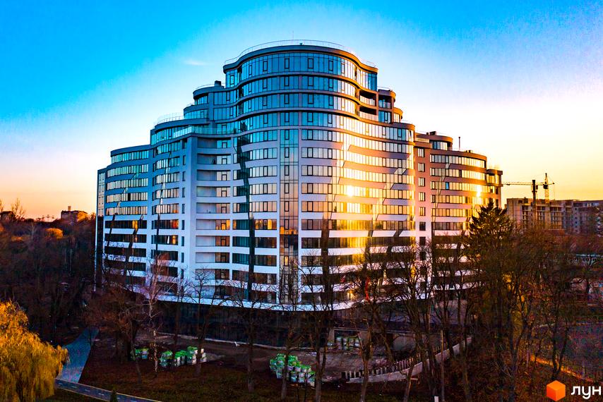 Зображення фасаду Житлового комплексу Parus. Багатоповерхова будівля з панорамними вікнами, навколо дерева та зелені на прибудинковій території.