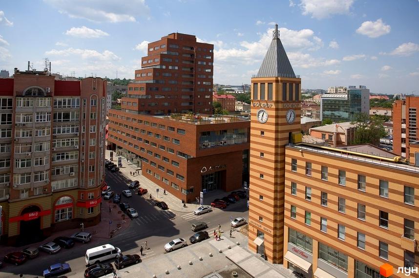 БФК „Дом на Катеринославском“: багатоповерховий комплекс з теракотовими фасадами, ступінчастою архітектурою та годинниковою вежею. Поруч проїжджа частина з автомобілями.