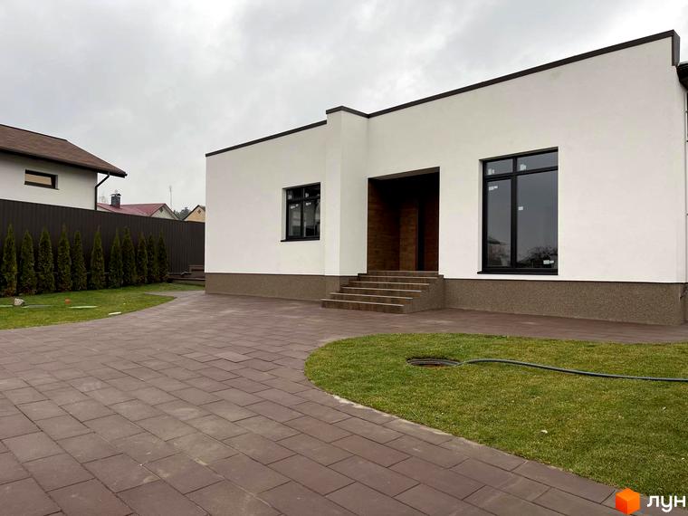 Котеджне містечко КМ White Stone: білий будинок з темними вікнами та коричневим цоколем, вимощена доріжка та зелена галявина.