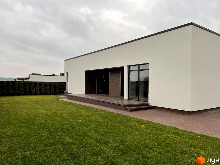 Котеджне містечко КМ White Stone: білий одноповерховий будинок з великими вікнами та терасою, зелений газон та дерева.