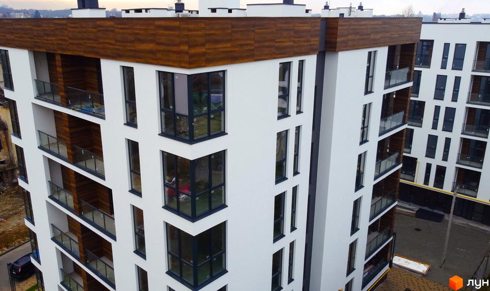 Висотна будівля ЖК Globus Central Park з білими фасадами та панорамними вікнами, коричневим оздобленням верхнього поверху. На території є парковка та зелені насадження.