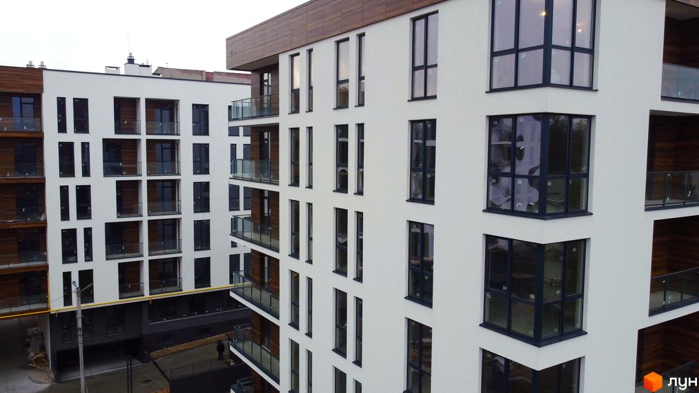 Білосніжний багатоповерховий будинок ЖК Globus Central Park з панорамними вікнами та скляними балконами. Видно частину прибудинкової території.