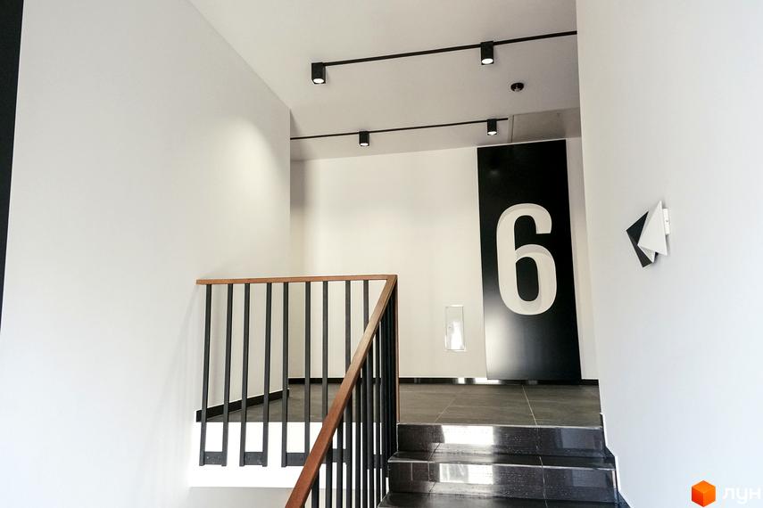 Сходи в новому будинку ЖК Globus Central Park з великим номером 6 на стіні. Чорні перила та білі стіни створюють контрастний дизайн.