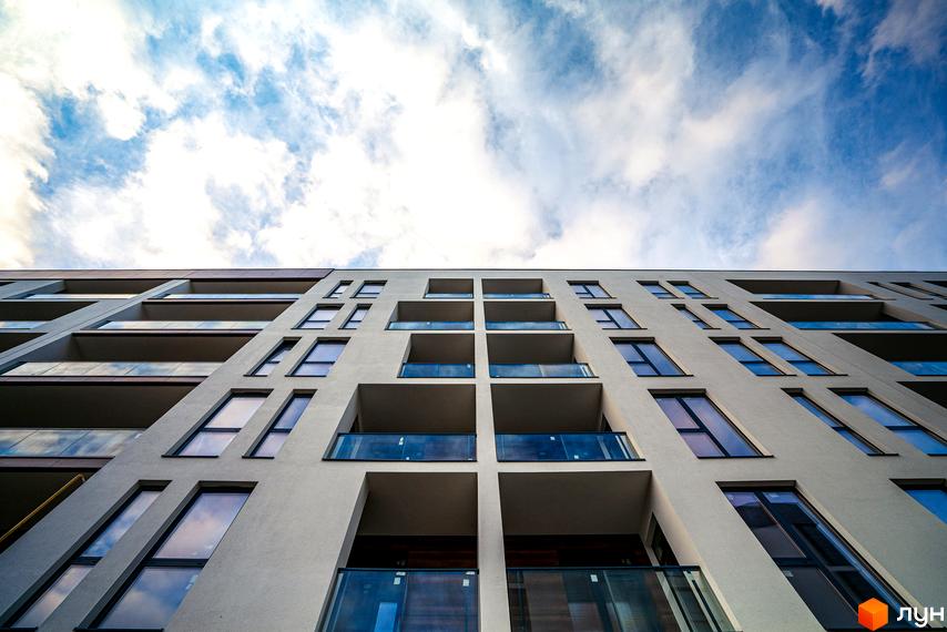 Висотна новобудова ЖК Globus Central Park з балконами та панорамними вікнами на фоні блакитного неба з хмарами.