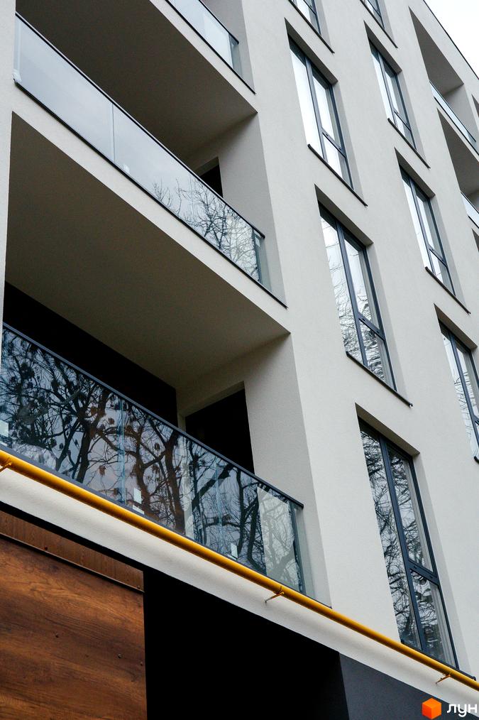 Фасад багатоповерхового будинку ЖК Globus Central Park з панорамними вікнами та скляними балконами. На балконах відображаються дерева.