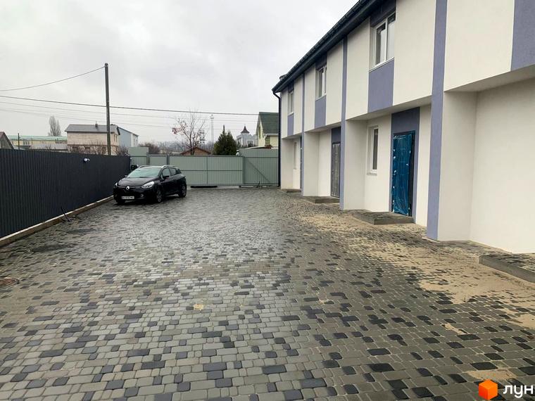 Зовнішній вигляд таунхаусів Smart Country House 2 з білими стінами та сірими вставками. На подвір'ї викладена плитка та стоїть автомобіль.