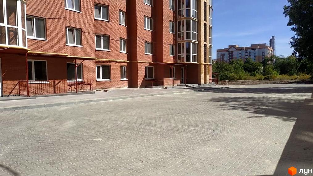 Фасад цегляного житлового комплексу з білими вікнами та заскленими лоджіями. Перед ним вимощена прибудинкова територія на вул. Київська.