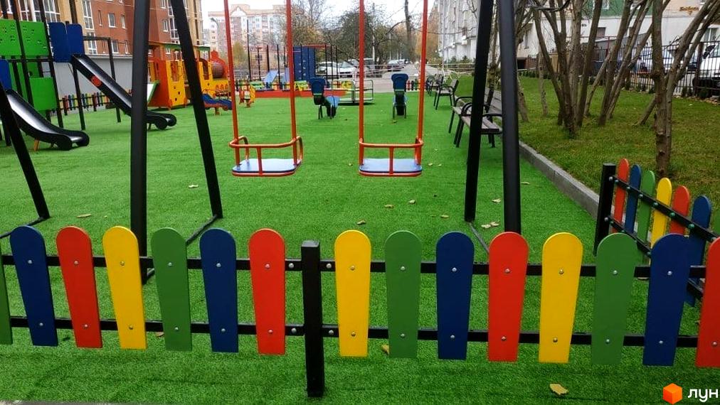Багатоповерховий житловий комплекс на вул. Київська. Прибудинкова територія має дитячий майданчик з гойдалками та гірками на зеленому покритті.