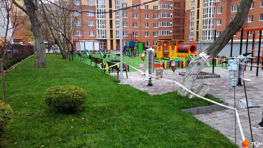 Багатоповерховий житловий будинок з цегли на вул. Київська та облаштований дитячий майданчик з зеленим газоном.