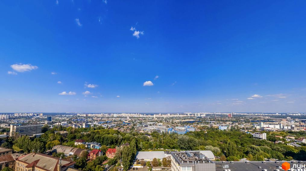 Вид на місто з висоти пташиного польоту. На передньому плані розташовані будинки різної поверховості, навколо зелені насадження. На горизонті видно багатоповерхові будівлі.