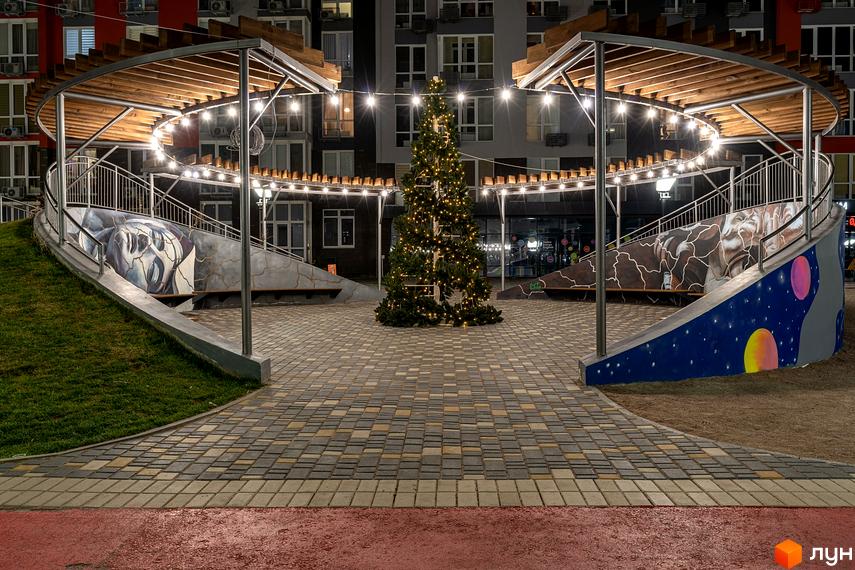 Багатоповерхові будинки Котеджного містечка ARTVILLE вночі. Внутрішній двір з ялинкою, освітленою гірляндами, круглою перголою та розписаними стінами.