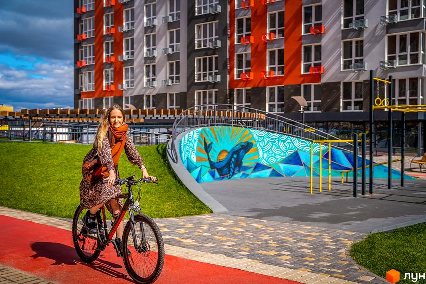 Багатоповерховий будинок Житлового містечка ARTVILLE з контрастними фасадами. Прибудинкова територія має велодоріжку, зелені газони та яскравий мурал.