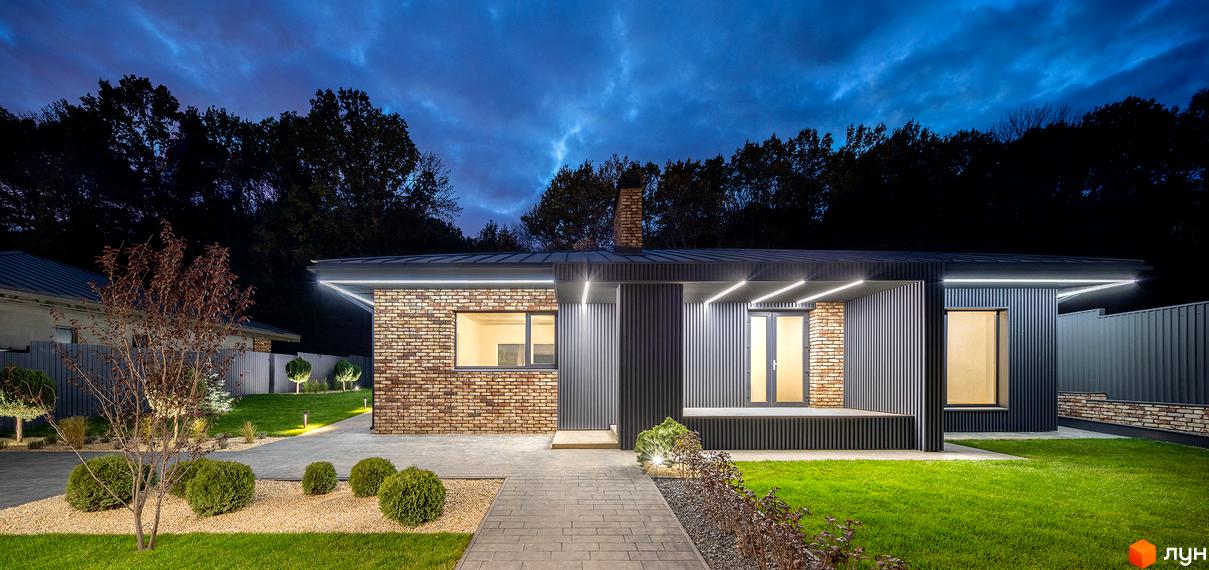 Зовнішній вигляд будинку з цегляними та металевими елементами. Перед будинком доглянутий газон та доріжка з бруківки.