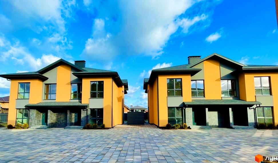 Сучасні дуплекси Карамель Сіті з жовто-сірими фасадами та великими вікнами на бруківці під блакитним небом.