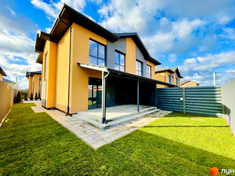 Двоповерховий дуплекс Карамель Сіті з оранжевим фасадом та сірими елементами, прибудинкова територія з доглянутим газоном та бруківкою.