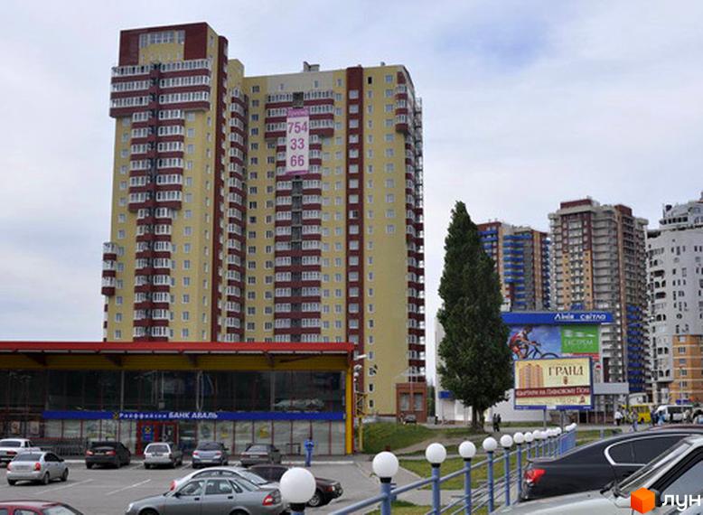 Житловий комплекс Тріумф з фасадом жовтого кольору та балконами. Прибудинкова територія з паркувальними місцями та зеленими насадженнями.