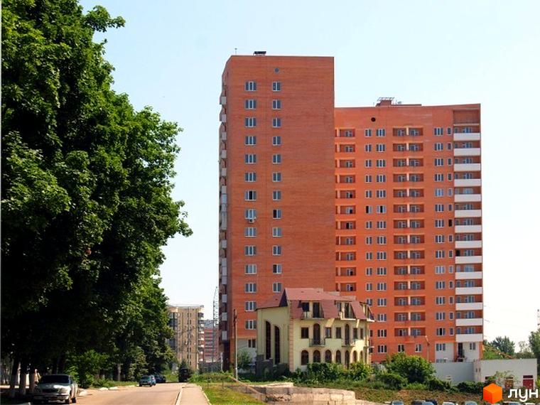 Житловий комплекс ЖК Гранд з висотним будинком оранжевого кольору на фоні зелених дерев та прибудинкової території.