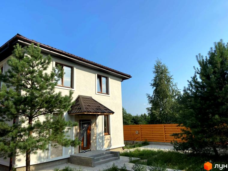 Зображення будинку в Котеджному містечку Vita House з коричневим дахом та вікнами. Навколо зелені дерева та доглянута територія.