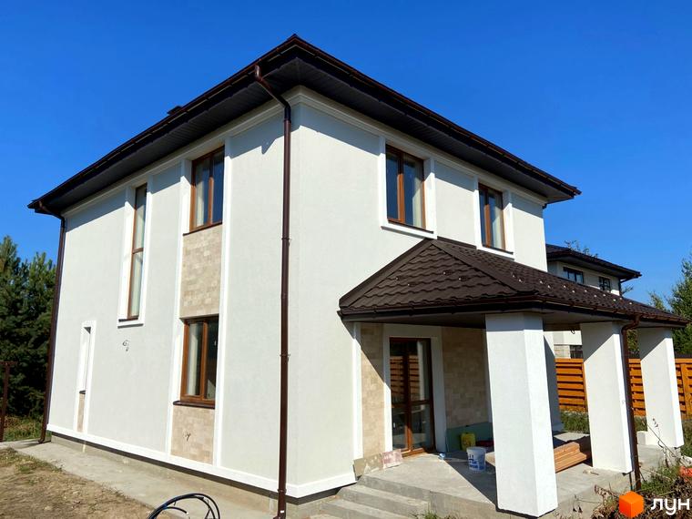 Зовнішній вигляд двоповерхового будинку в Котеджному містечку Vita House з коричневим дахом та вікнами. Навколо будинку зелена трава.