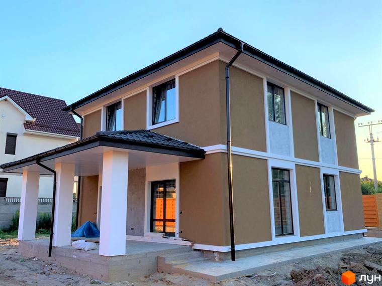 Двоповерховий будинок в Котеджному містечку Vita House з коричневим фасадом, білими колонами та вікнами, на тлі блакитного неба.